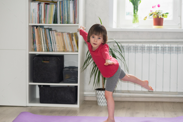 Child girl performs the exercise gymnastics at home on a mat
