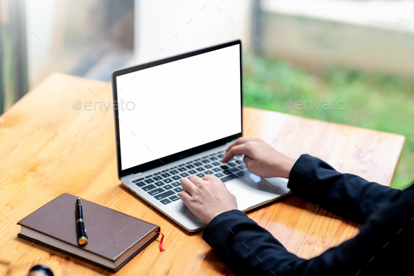Businesswoman working using laptop keyboard blank white screen with notebook and pen on desk.