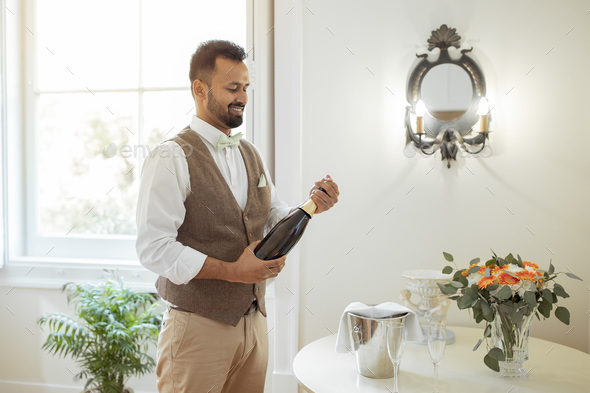 Cheerful Waiter Man Opening Bottle Of Wine In Hotel Room