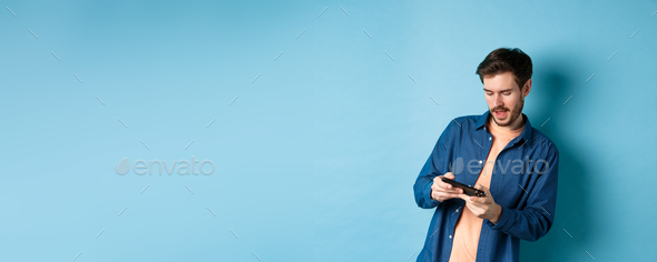 Young guy playing video game on mobile phone, tilt body and holding smartphone horizontally