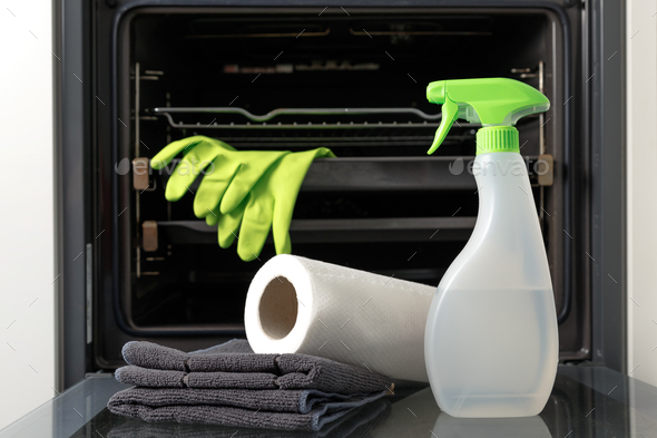 Oven cleaner kit on open door. Bottle with ecological health-friendly detergent, wipes and gloves