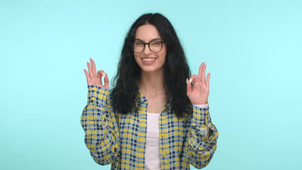 Cheerful Pretty Woman with Long Curly Hair Wearing Glasses and Casual Shirt Showing Ok Sign Saying
