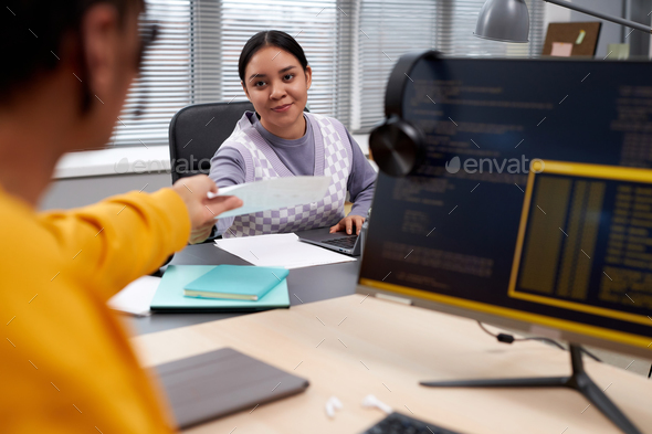 Two young people working in IT development and handing documents across table