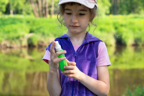 Girl sprays mosquito spray on the skin in nature that bite her hands and feet. Protection from insec