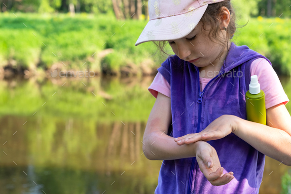 Girl sprays mosquito spray on the skin in nature that bite her hands and feet. Protection from insec