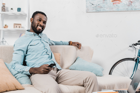 happy african american man sitting on couch with remote controller