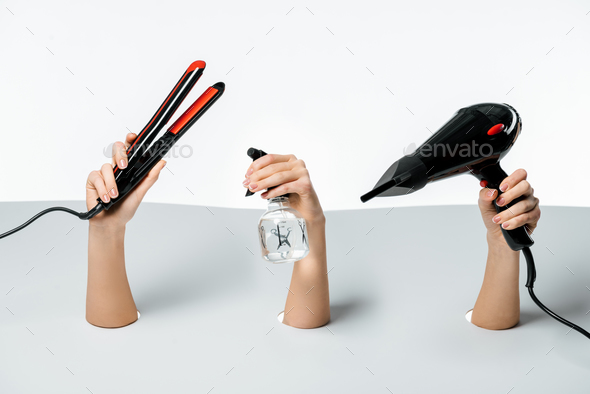 partial view of women holding hairstyle tools through holes on white