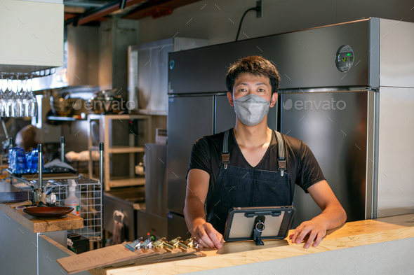 A man wearing a face mask at the counter of a restaurant kitchen