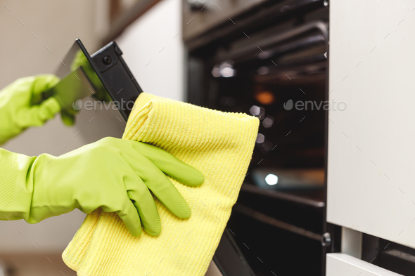 Hand in Green Glove Cleaning Kitchen Oven Door with Microfiber Rag. Doing Home Chores