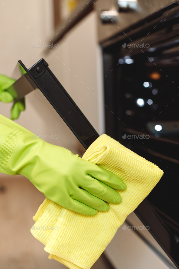 Hand in Green Glove Cleaning Kitchen Oven Door with Microfiber Rag. Doing Home Chores