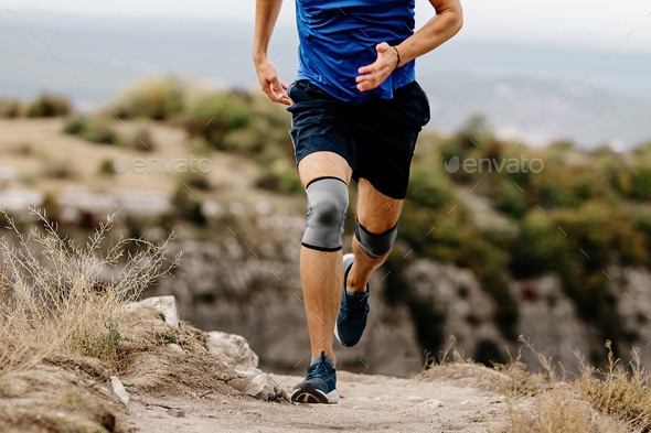 male runner with knee pads running on mountain trail
