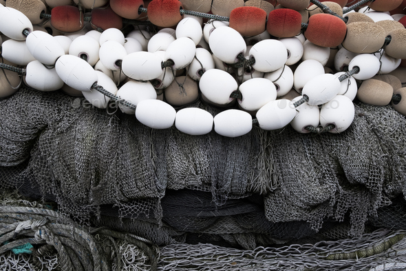 A pile of commercial fishing nets on a quay, white and red plastic floats  and nets and ropes. Stock Photo by Mint_Images