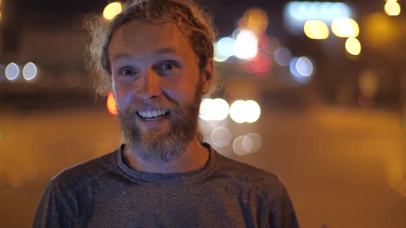 Smiling Handsome Caucasian Bearded Long-haired Young Man Looks Straight To the Camera and Shows alt