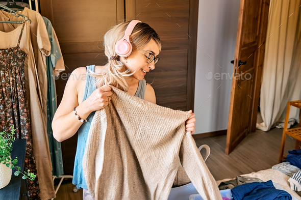 Woman in headphones listening music, dancing and singing while making order of clothes