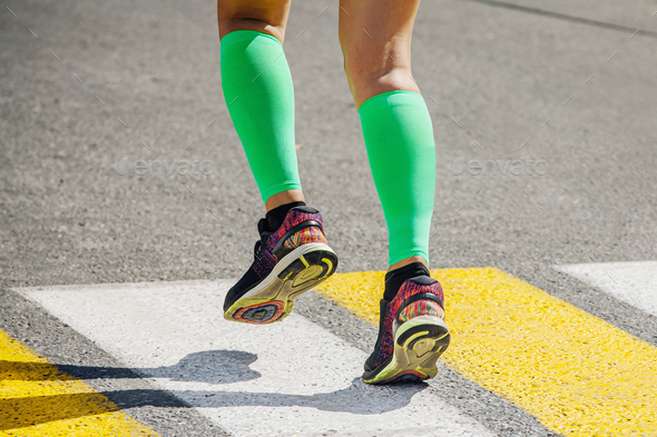legs female runner in bright green compression socks running pedestrian crossing on road