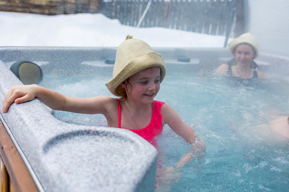 Cheerful happy family with children enjoys hot bath in jacuzzi whirlpool on cold winter day