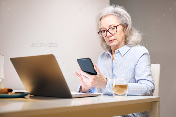 Serious lady with glasses settled down with laptop at kitchen table