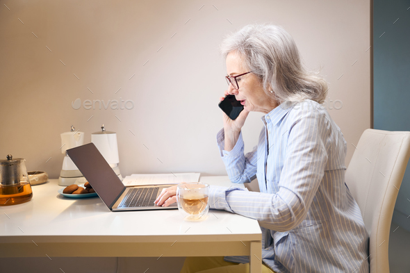 Modern elderly lady works from home, she communicates on phone