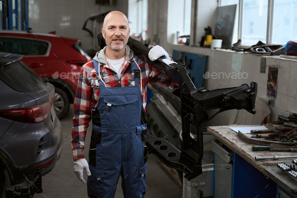 Fit middle-aged man holds car body part on his shoulder