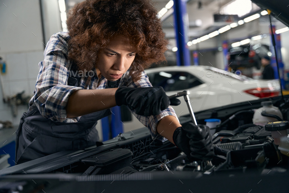 Woman auto mechanic repairs car in modern auto repair shop