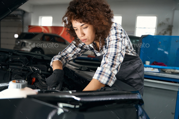 Prettyl woman is repairing car in modern auto repair shop