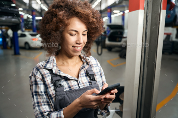Employee of a modern auto repair shop holds mobile phone