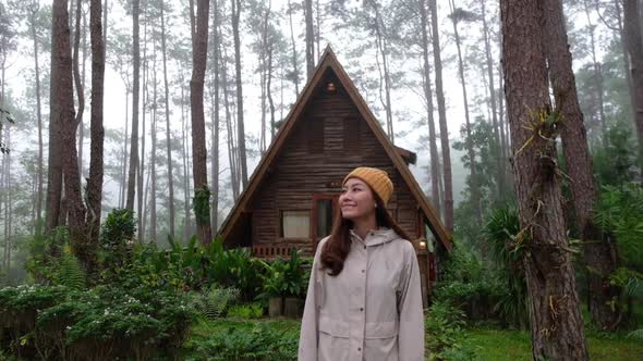 Slow motion of a young woman standing in front of a log cabin in the woods