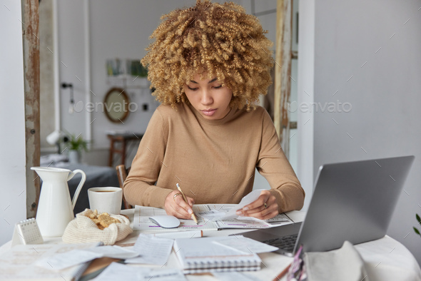 Photo of serious busy woman makes notes studies bills reads paper invoice develops personal budget