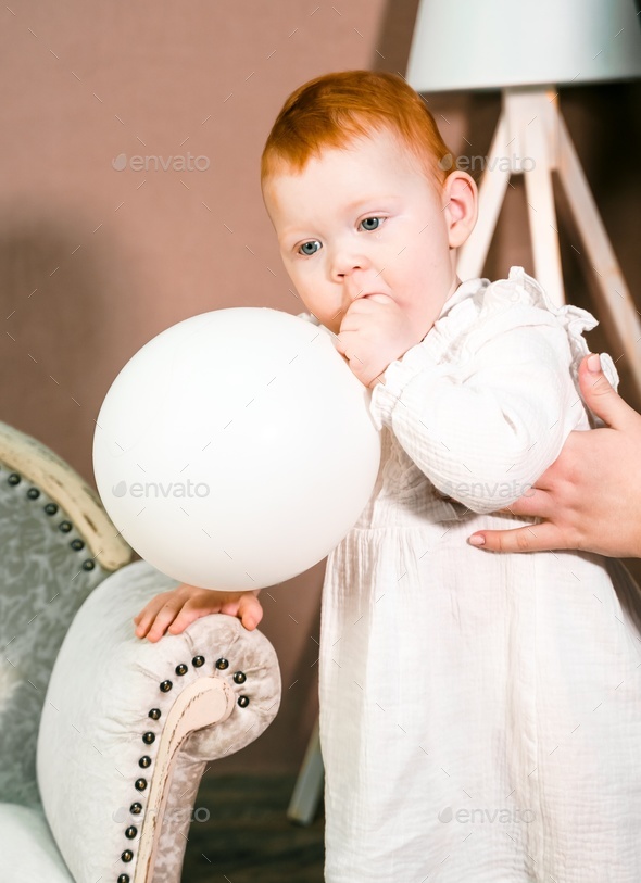 Little redhead baby girl wih balloon celebrates first birthday anniversary. 1 year family party
