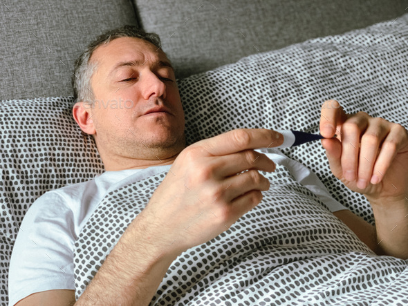 Middle aged man is sick at home, having flu or hangover. Middle aged man is in bed having flu covid