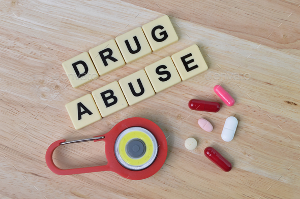 Top view of pill capsules, toy padlock and square letters with text DRUG ABUSE.