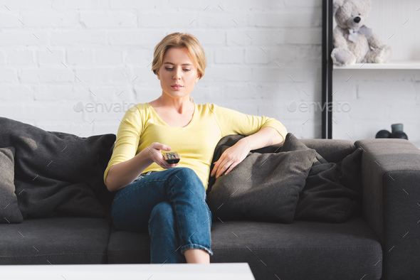 attractive woman sitting on couch and using remote controller