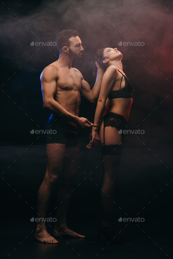 beautiful passionate couple with handcuffs in smoky room