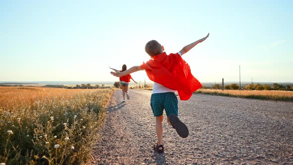 Two Running Children in Field Under Sunlight Brother and Sister Put Homemade Superheroes Costumes alt