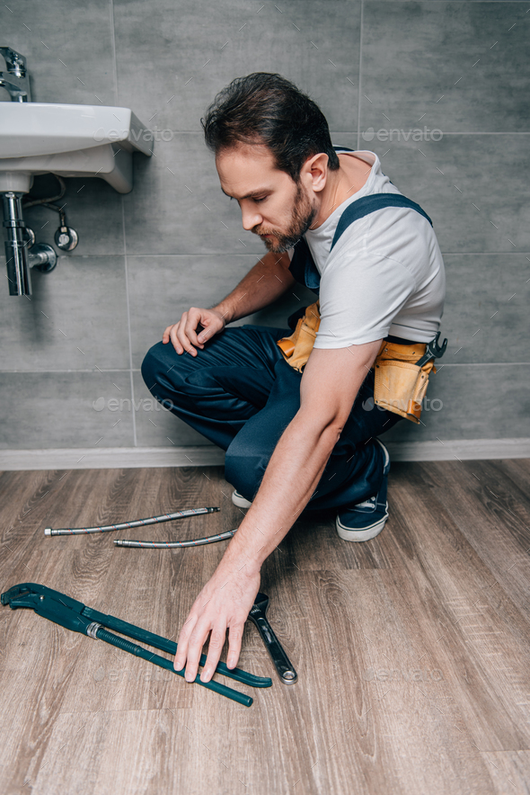 adult male plumber taking gas wrench for repairing broken sink in bathroom