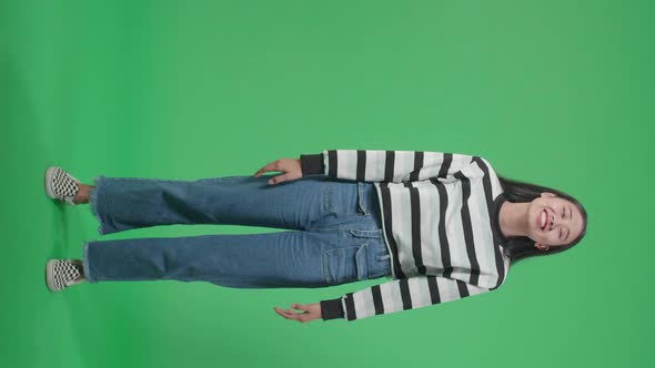 Full Body Of A Smiling Asian Woman Dabbing While Standing In Front Of Green Screen Background alt
