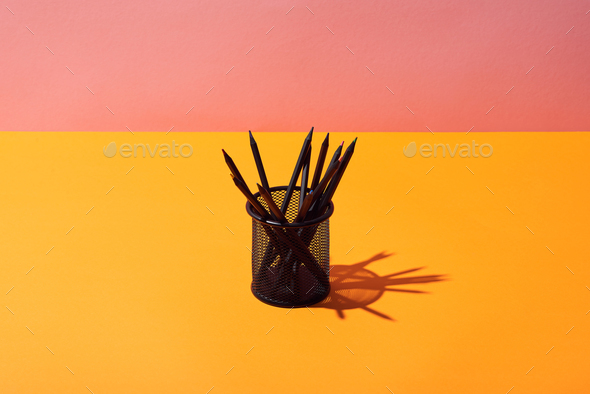 pencil holder with pencils on yellow surface and pink background