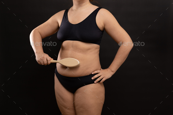 Plus size woman in black underwear massaging belly with brush. Flaunt  figure imperfections. Dry anti Stock Photo by burmistrovaiuliia