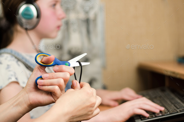 Female hands are cutting the headphone cord with scissors, in the background is a girl in headphones
