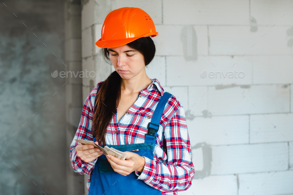 female worker holding dollar bills in hands and counts money on construction site