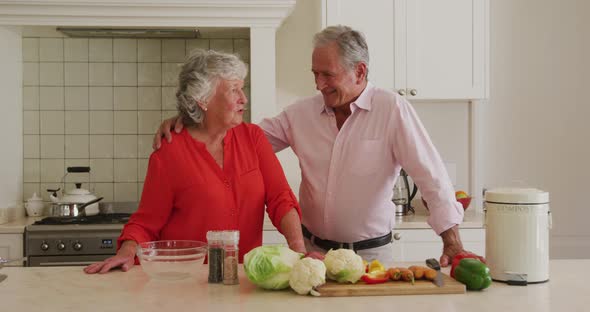 Portrait of caucasian senior couple embracing each other in the kitchen at home alt