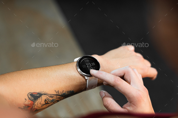 white index finger of right hand pointing a clock on tattooed left arm of young caucasian woman