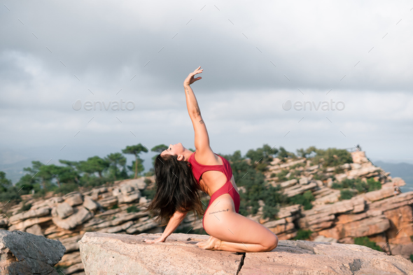 Caucasian mature woman doing gymnastics sitting on her heels with her left arm outstretched on a