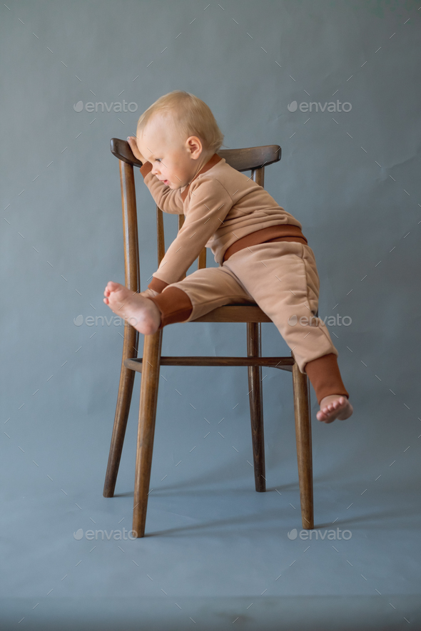  Portrait Cute one year old baby girl, wearing brown suit, sitting on a wooden chair. - Stock Photo - Images