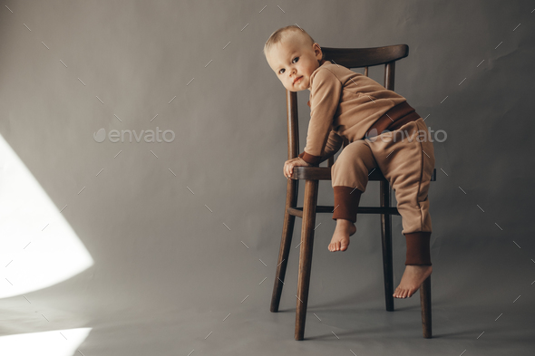  Portrait cute one year old baby girl, wearing brown suit, sitting on a wooden chair - Stock Photo - Images