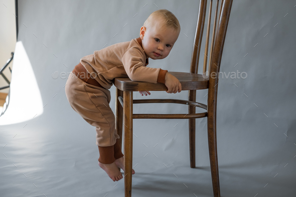 The kid hangs on a wooden chair, trying to climb on it - Stock Photo - Images