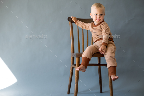 Portrait cute one year old baby girl, sitting on a wooden chair. - Stock Photo - Images