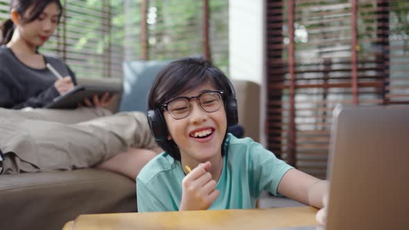Asian boy singing while doing homework with a laptop