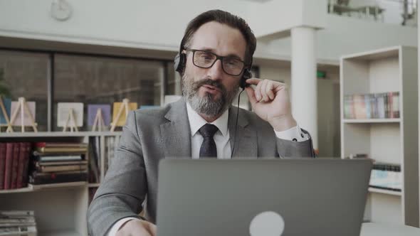 Middleaged Businessman Manager Wearing Earphones Holding Video Call Looking at Laptop Screen alt