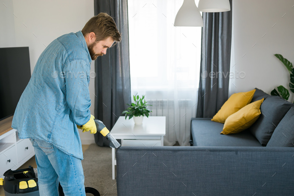 Man holding modern washing vacuum cleaner and cleaning dirty sofa with professionally detergent